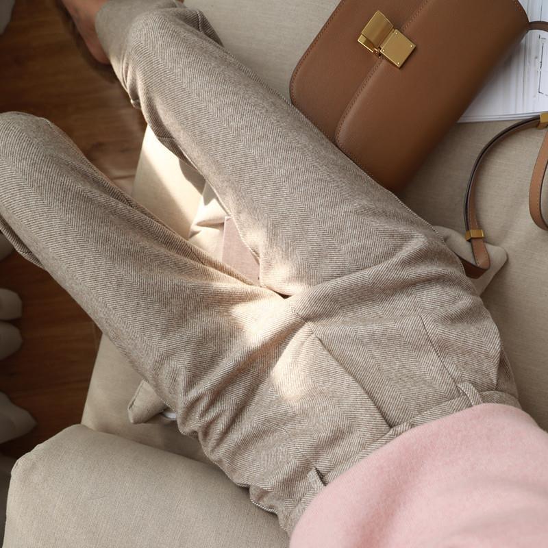Person wearing beige herringbone textured pants reclining on a beige sofa with a brown leather handbag nearby
