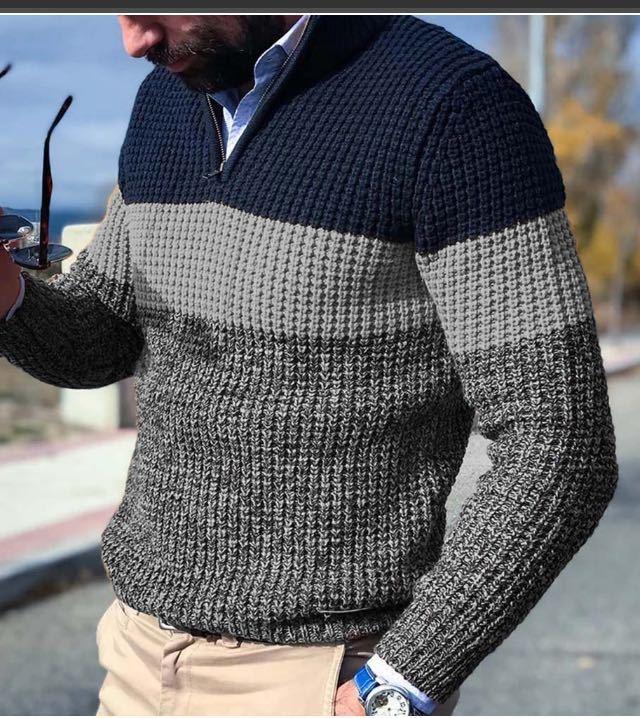 Man wearing textured knit sweater with navy, gray, and dark gray color blocks holding sunglasses outdoors