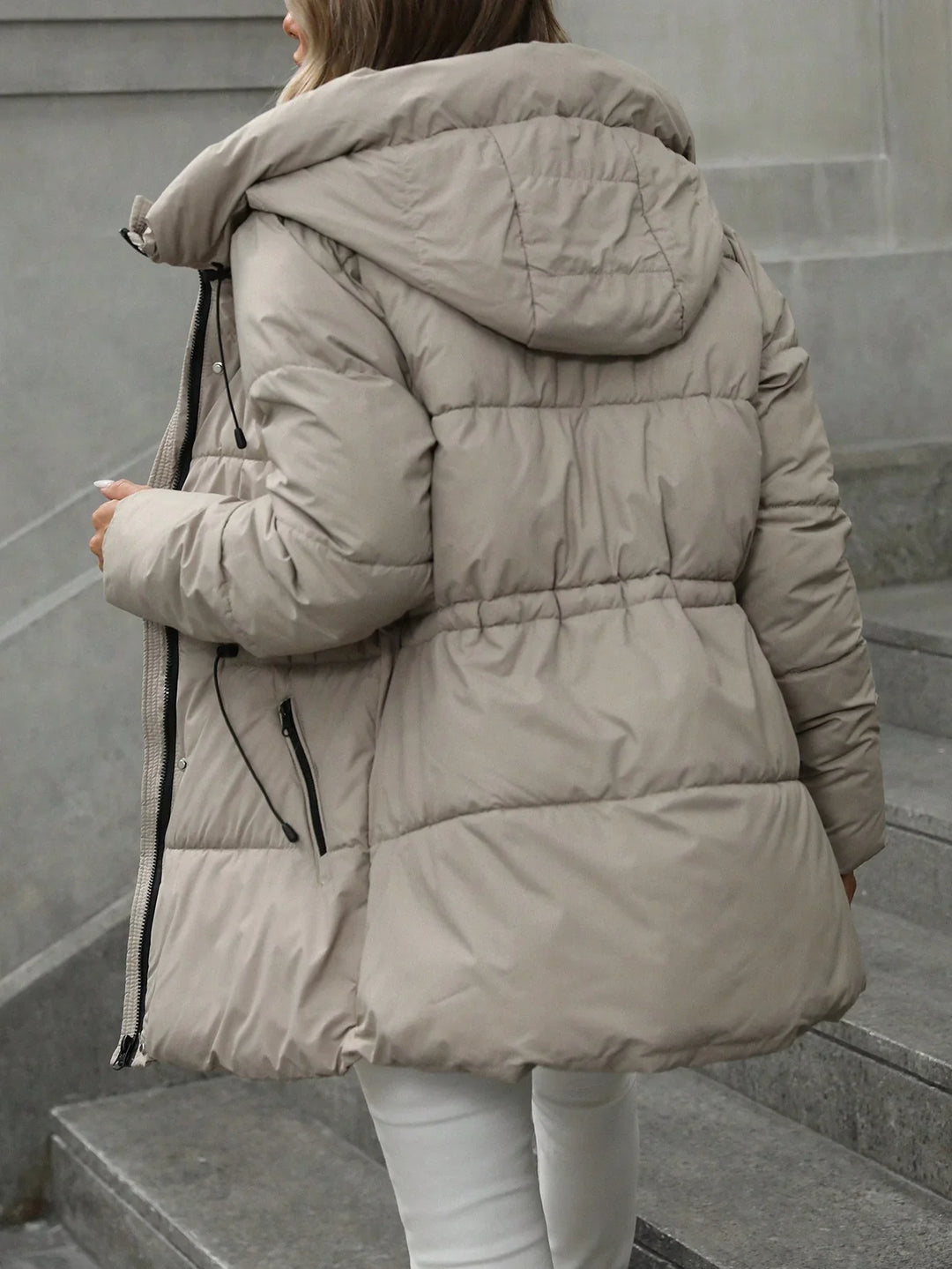 Woman wearing beige puffer jacket with hood walking up gray stone stairs outdoors