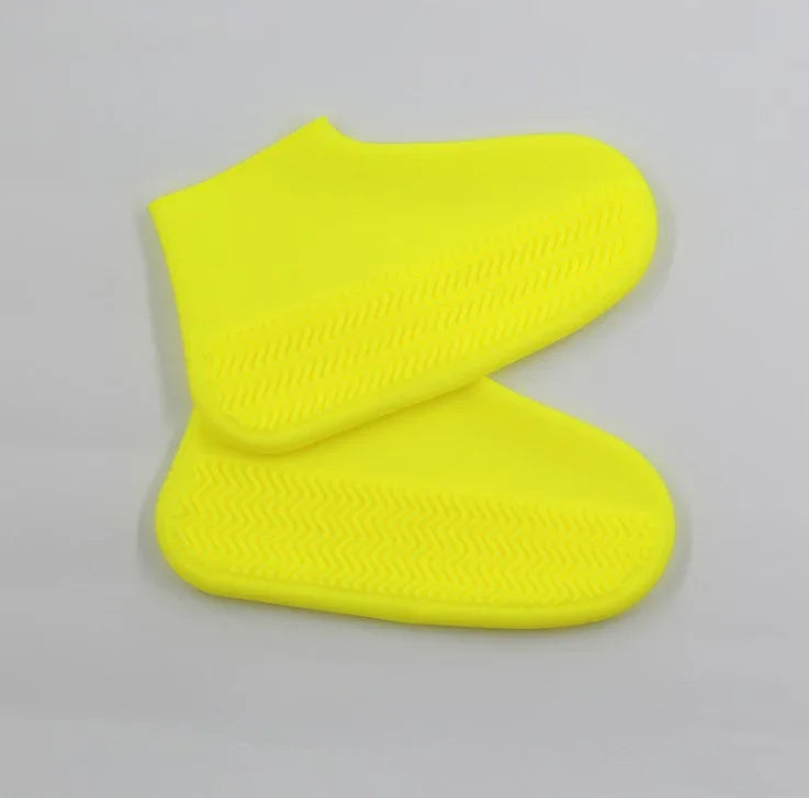 Pair of bright yellow silicone shoe covers with textured soles on gray background
