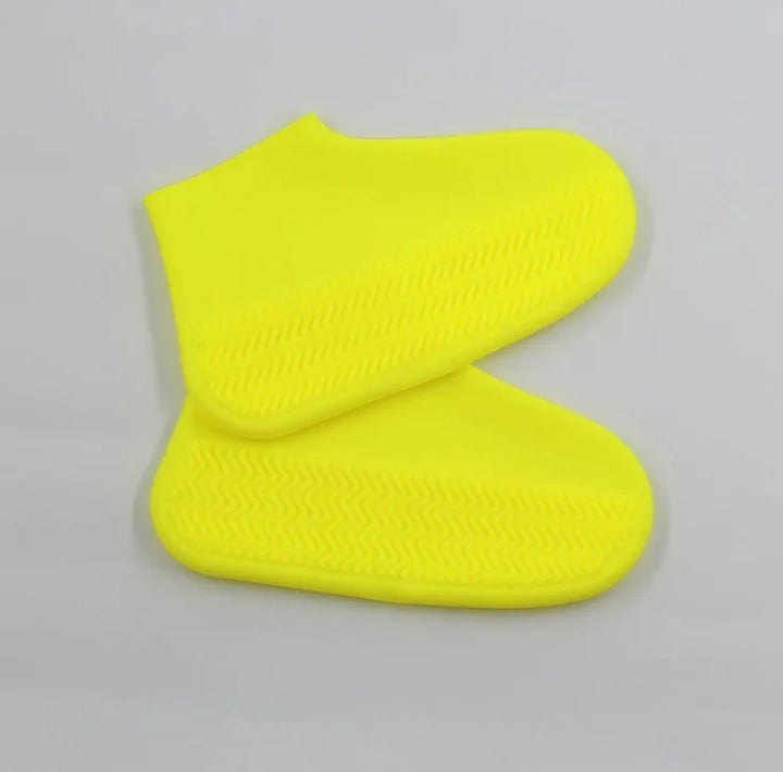 Pair of bright yellow silicone shoe covers with textured soles on gray background