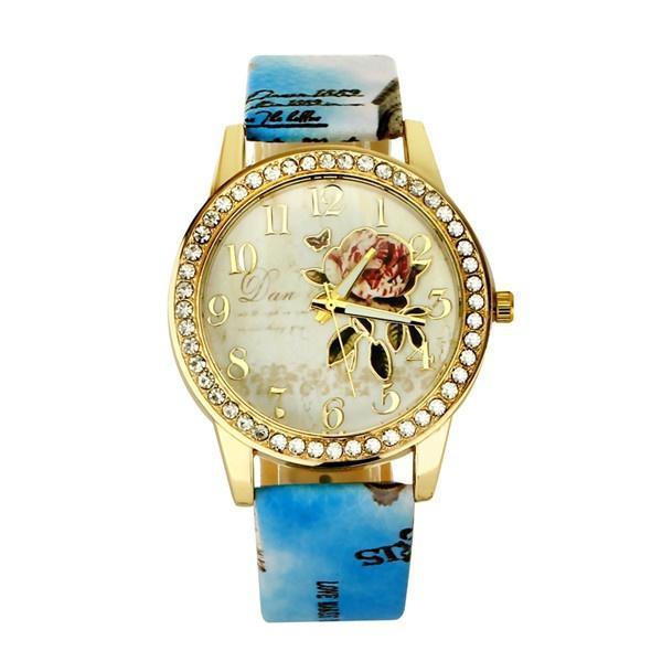 Gold-tone wristwatch with rhinestone bezel, floral dial, and blue patterned strap
