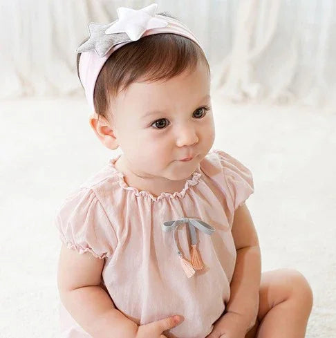 Cute baby girl wearing a pink headband with stars and a matching pink dress with tassels