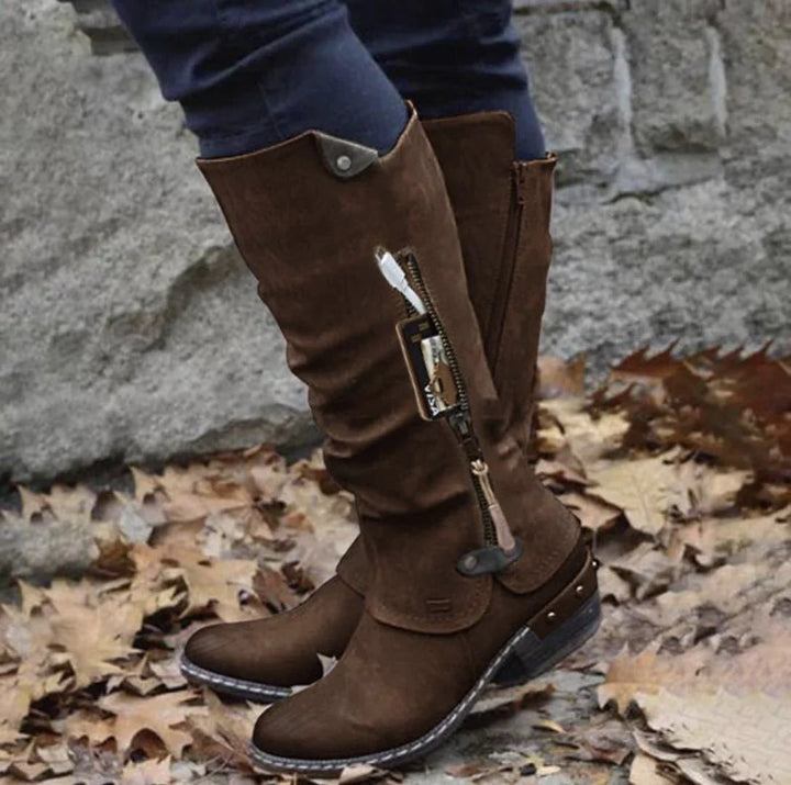 Brown suede knee-high women's boots with side zipper pocket holding card and USB cable outdoors