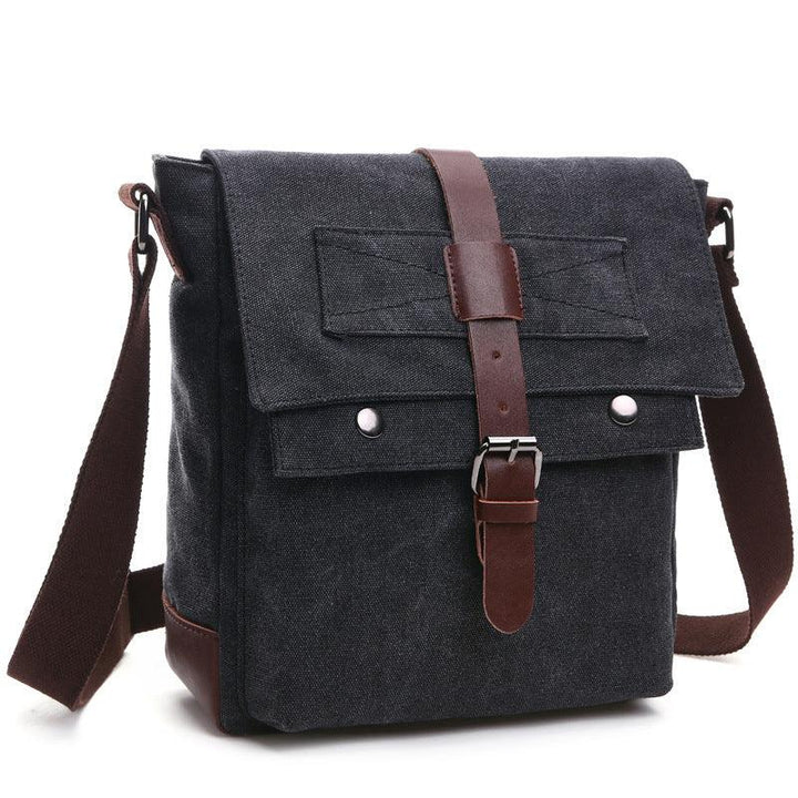 black canvas messenger bag with brown leather strap and silver buckles on white background