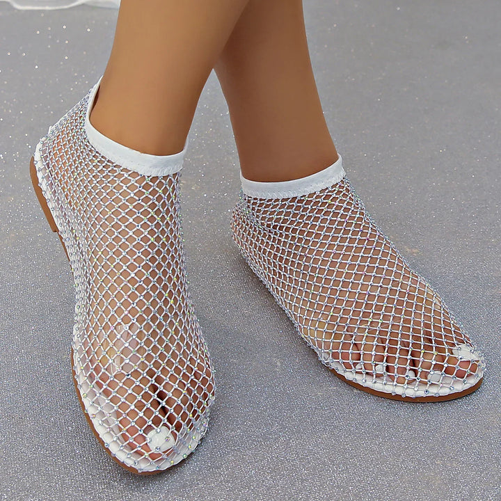 Feet wearing white mesh fishnet socks with rhinestone detailing on gray glitter background