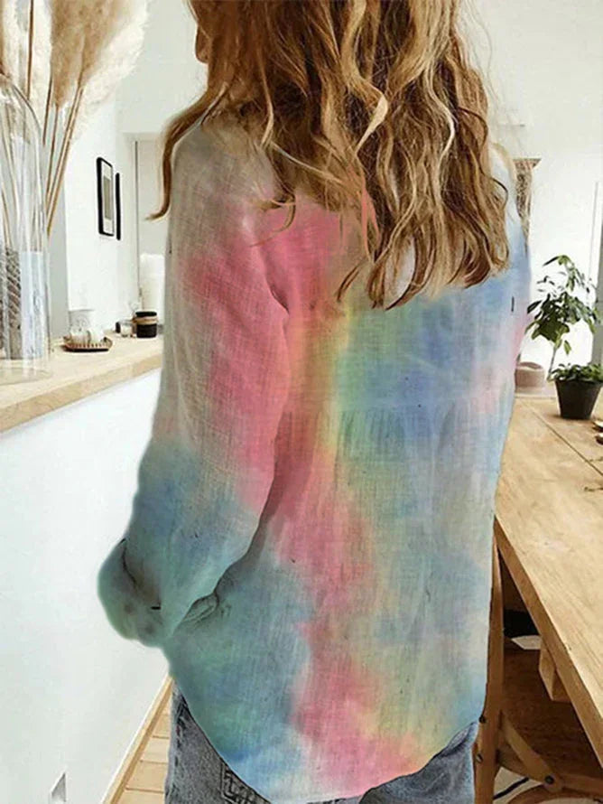 Woman wearing pastel tie-dye long sleeve shirt in cozy, modern room with wooden table and plants