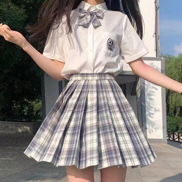 Girl wearing white short-sleeve shirt with bow and plaid pleated skirt outdoors