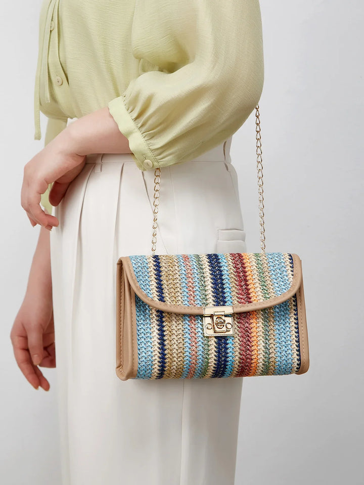 Woman wearing pale green blouse and white pants holding a colorful striped woven shoulder bag with gold chain