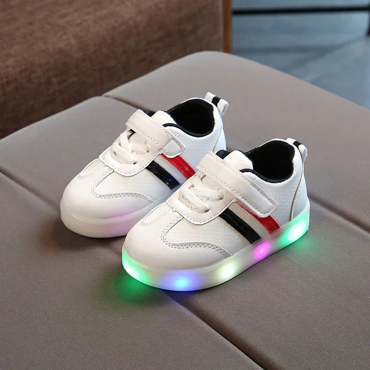 White children’s LED light-up sneakers with red and black stripes and Velcro straps on gray surface
