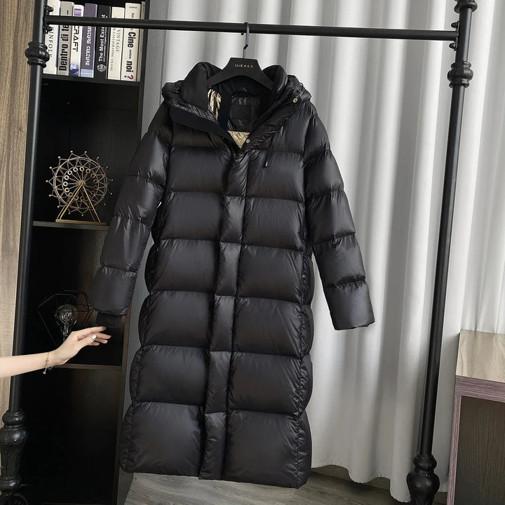 Long black puffer winter coat with hood hanging on a black metal rack in a modern room