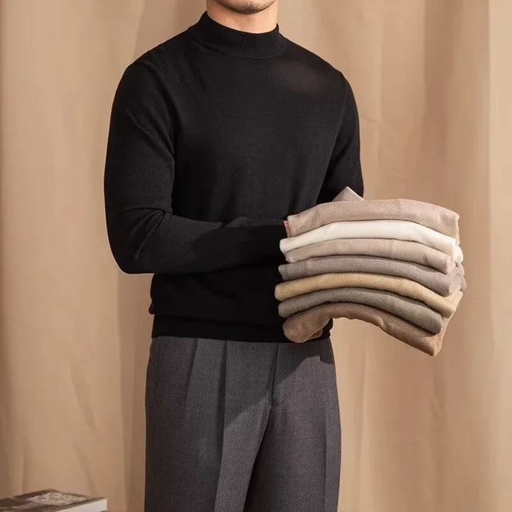 Man in black turtleneck holding folded sweaters in beige and neutral tones against beige background