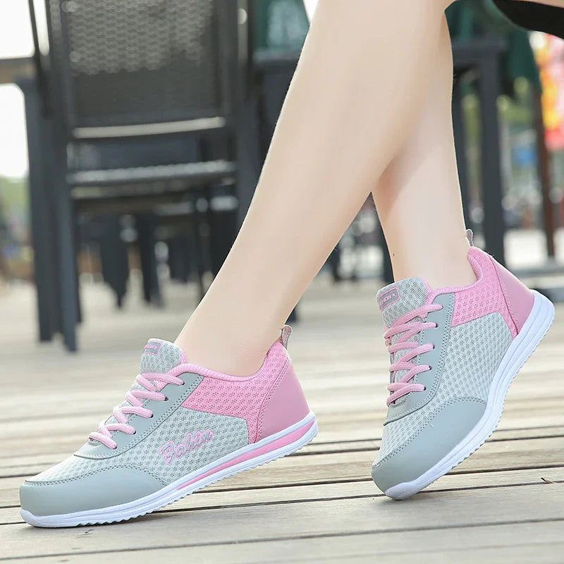 Light grey and pink breathable mesh sneakers with white soles worn outdoors on wooden deck