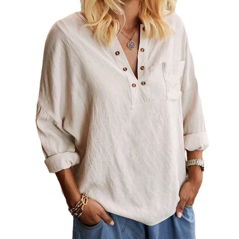 Woman wearing a loose white buttoned blouse with rolled sleeves and blue pants, accessorized with bracelets and a necklace