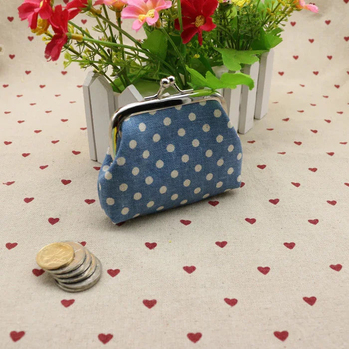 Blue polka dot coin purse with metal clasp on heart-patterned fabric beside stacked coins and flowers