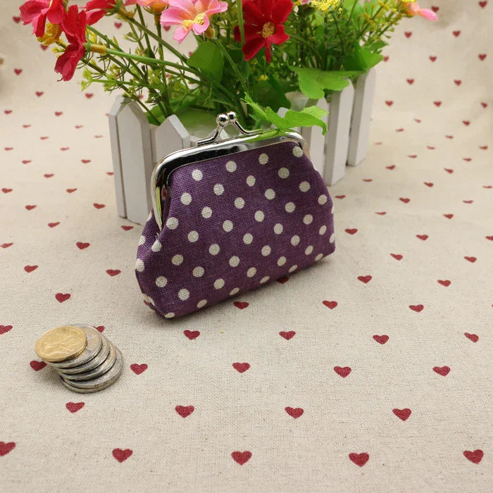 Purple polka dot coin purse with metal clasp on heart-patterned fabric with stacked coins and flowers