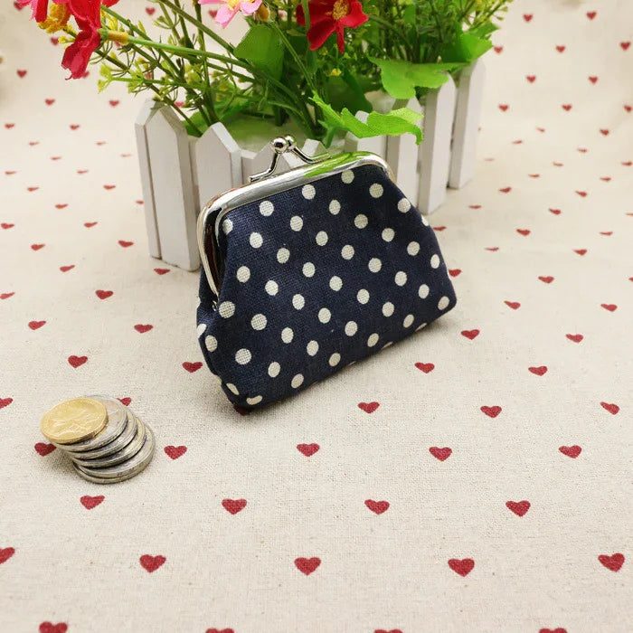 Navy blue polka dot coin purse with metal clasp on heart-patterned fabric next to stacked coins and flowers