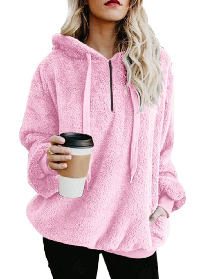 Woman wearing cozy pink fuzzy hoodie holding takeaway coffee cup with black lid
