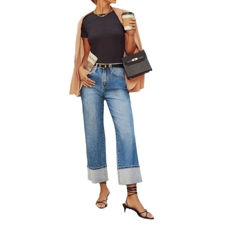 Woman wearing cuffed blue jeans, black top, beige blazer, strappy heels, holding coffee cup and black handbag