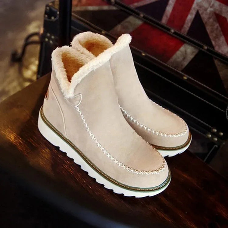 Beige ankle boots with white fluffy lining and stitched detailing on wooden surface