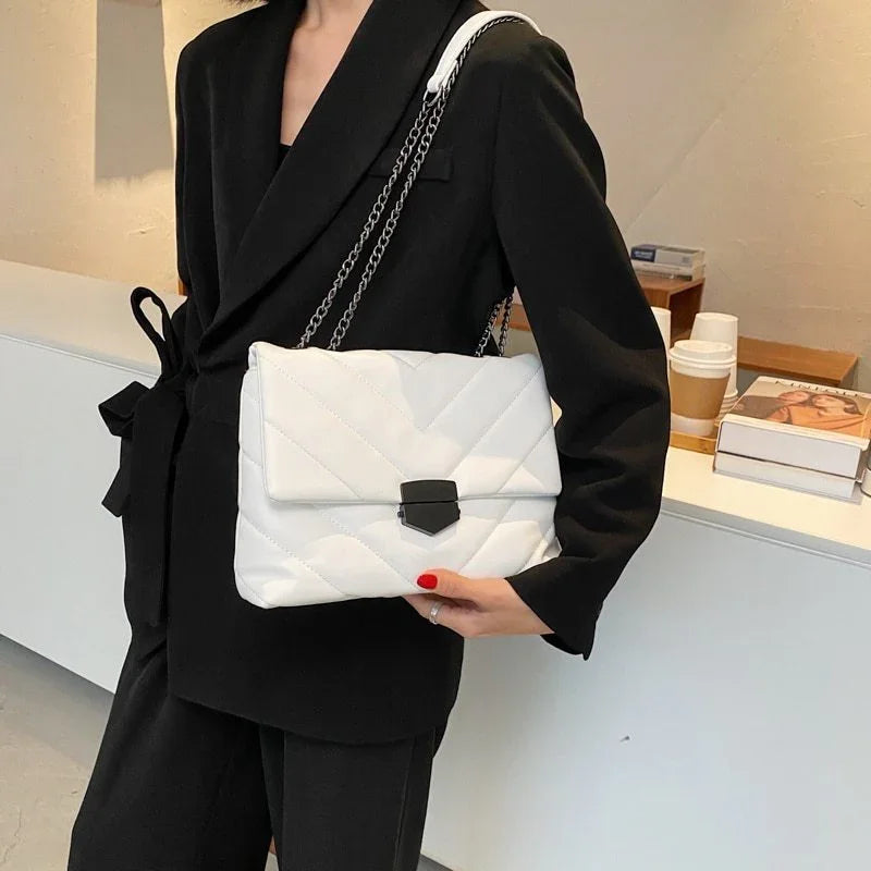 Woman in black blazer holding a white quilted chain shoulder bag with black clasp indoors