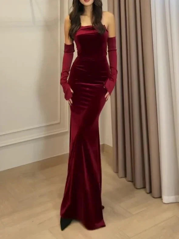 Woman wearing a floor-length burgundy velvet evening gown with matching long gloves, standing indoors