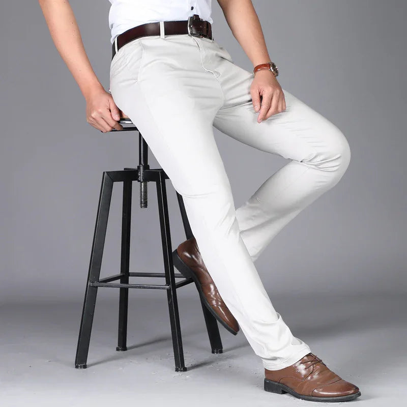 Man wearing slim fit white pants with brown leather belt and shoes sitting on black metal stool
