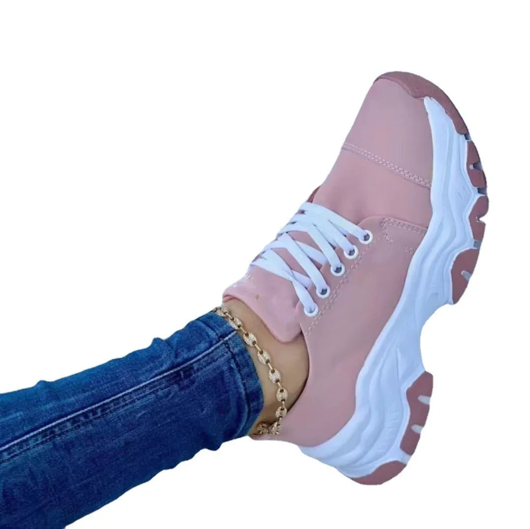 Person wearing pink chunky sneakers with white laces and blue jeans against white background