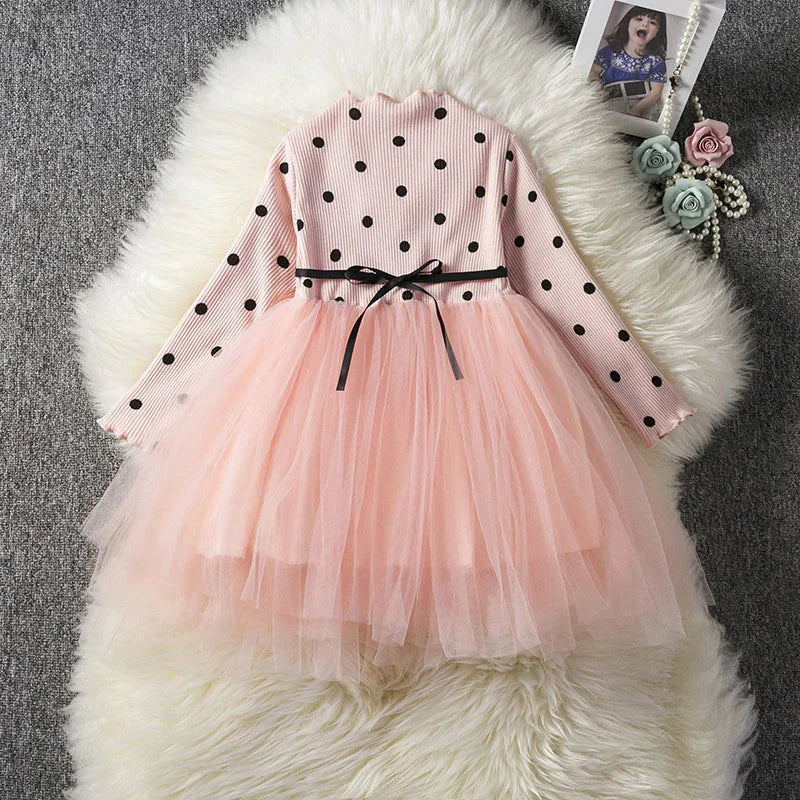 Pink long-sleeve girls dress with black polka dots, black ribbon belt, and layered tulle skirt on white fur