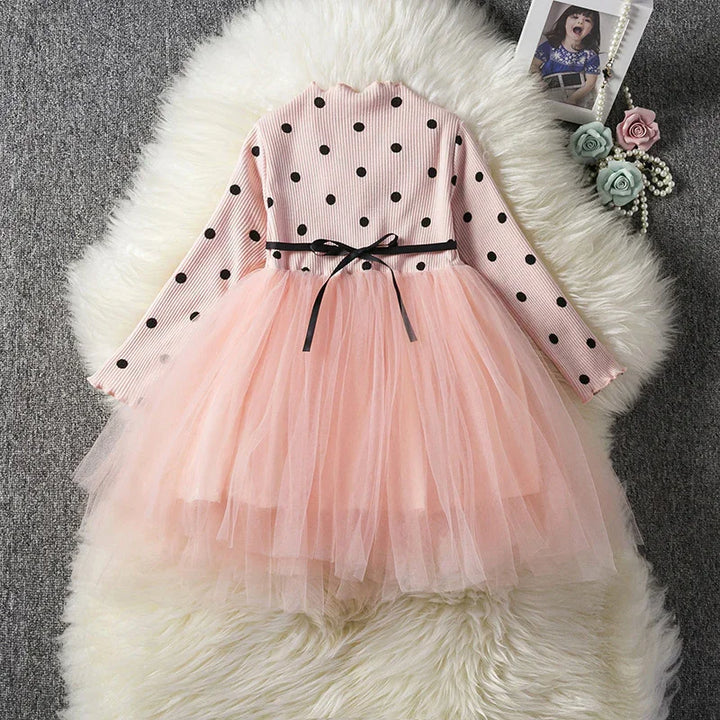 Pink long-sleeve girls dress with black polka dots, black ribbon belt, and layered tulle skirt on white fur