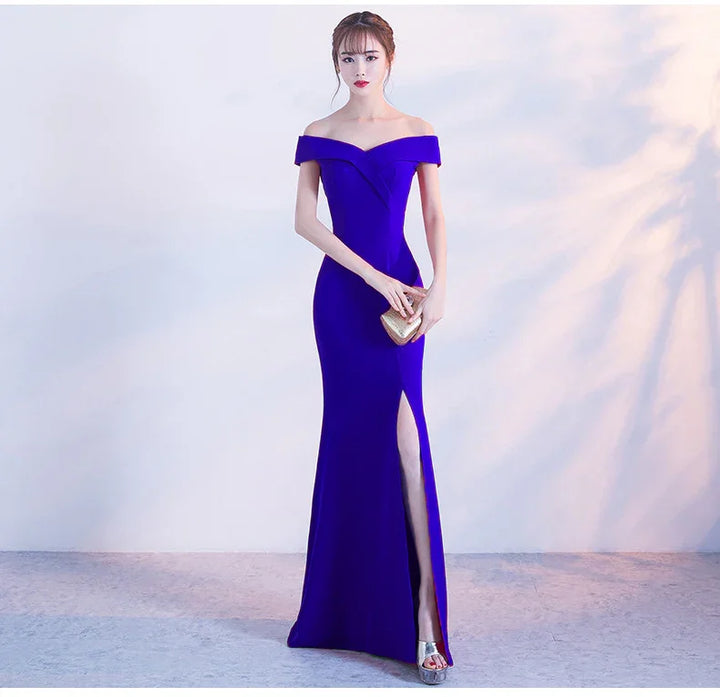 Woman in elegant royal blue off-shoulder evening gown with thigh slit holding a gold clutch