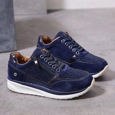 Navy blue suede sneakers with decorative studs, side zipper, and white soles on gray floor
