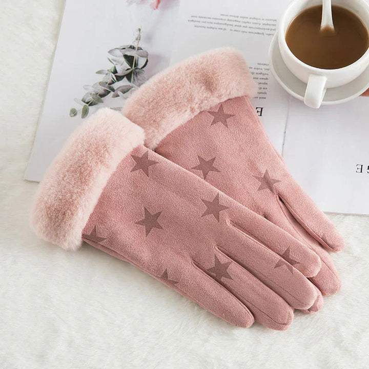 Pink winter gloves with star patterns and plush cuffs placed on a white surface next to a cup of coffee