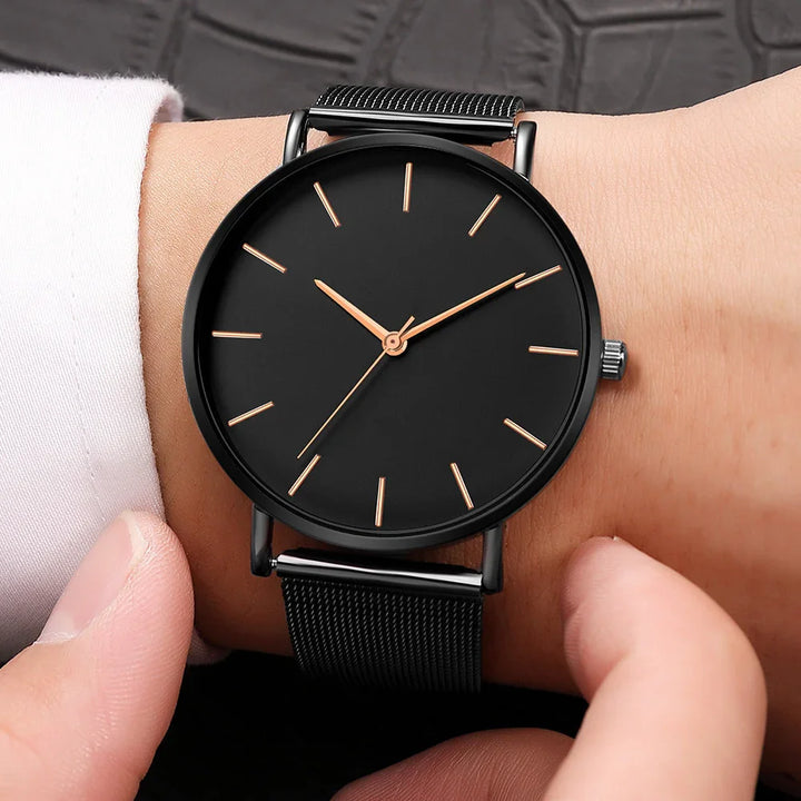 Minimalist black wristwatch with gold hour markers and mesh strap on wrist