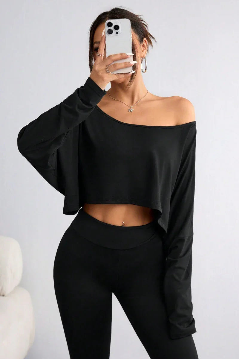 Woman wearing black off-shoulder crop top and black leggings taking a mirror selfie