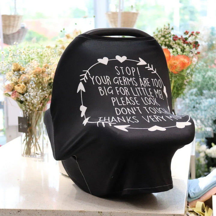 Black baby car seat cover with white protective message text surrounded by flowers on a countertop