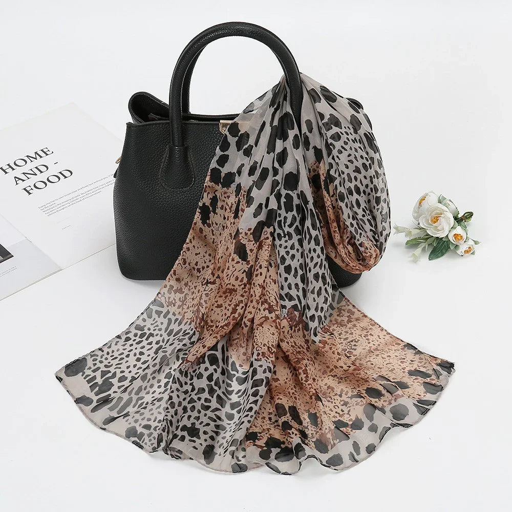 Black leather handbag with brown and gray leopard print scarf draped over it, white flowers nearby