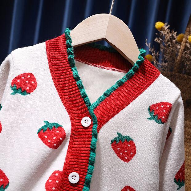 White cardigan with red strawberries and green trim hanging on wooden hanger