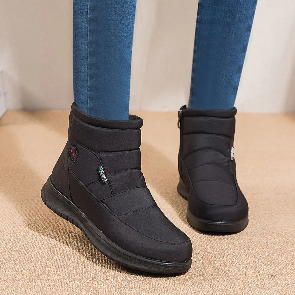 Black insulated winter boots with side zipper and sporty label, worn with blue jeans on beige carpet