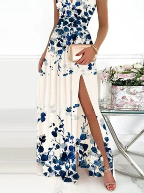 Elegant white maxi dress with blue floral print and high slit, accessorized with beige clutch and bracelet