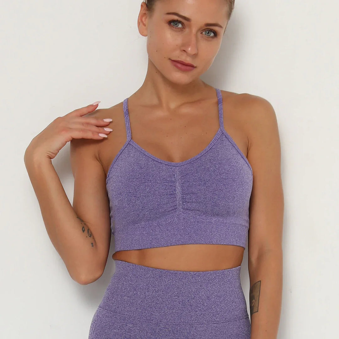 Woman wearing purple seamless sports bra and matching high-waisted leggings against white wall