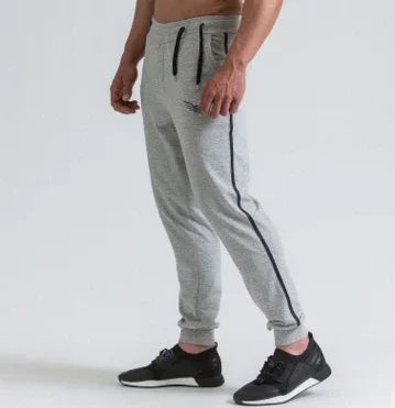 Man wearing grey jogger pants with black side stripe and black sneakers on white background