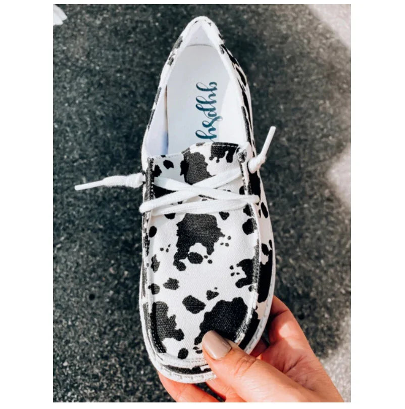 Hand holding a black and white cow print casual canvas shoe with white laces on asphalt background