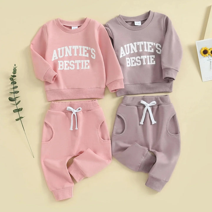 Two baby outfit sets in pink and mauve with "AUNTIE'S BESTIE" text, cozy long sleeves and pants