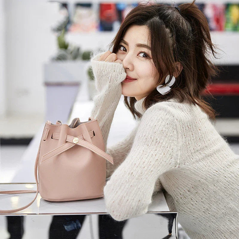 Young woman in cozy knit sweater posing with stylish pink leather bucket bag indoors