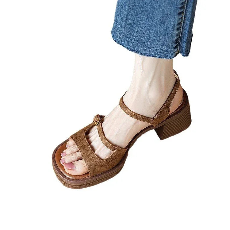 Close-up of foot wearing brown block heel sandal with ankle strap and buckle, paired with blue jeans