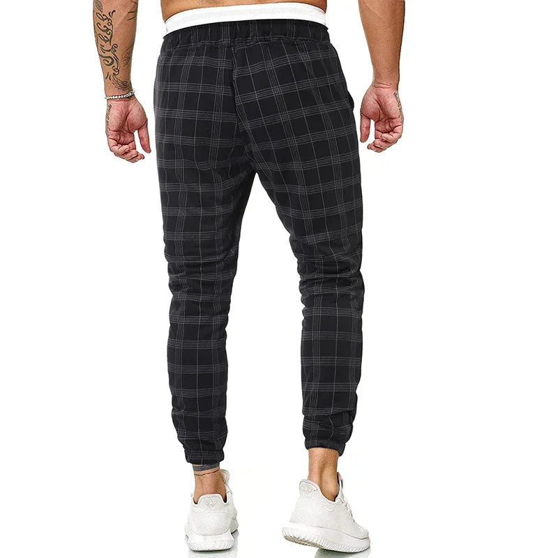 Man wearing black plaid jogger pants with elastic cuffs and white sneakers, back view