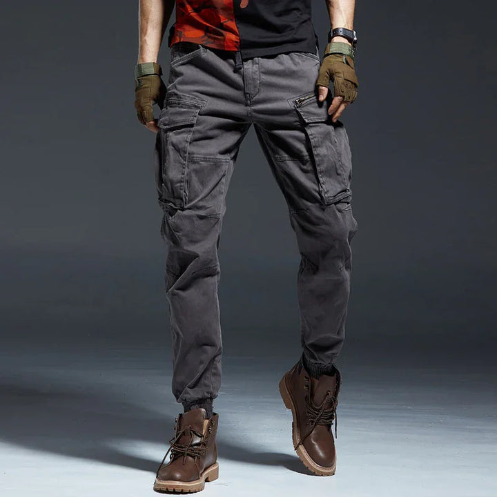 Men's grey cargo pants with multiple pockets, worn with brown leather boots and fingerless gloves