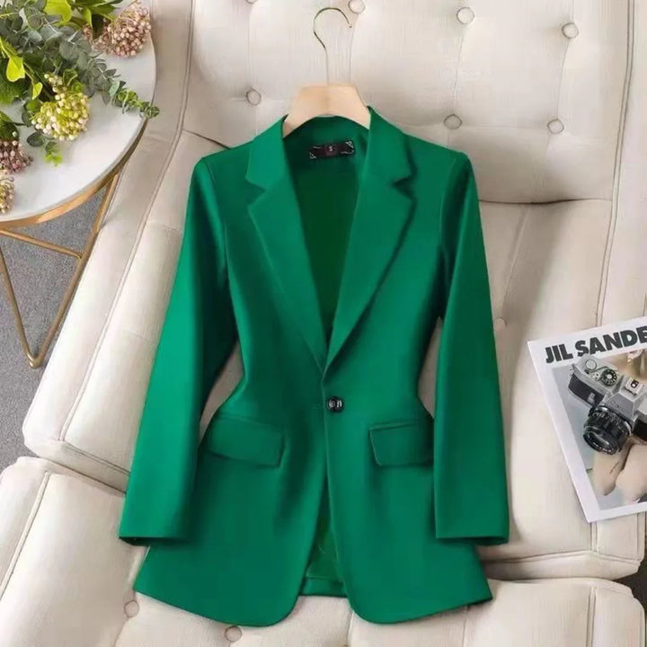 Green single-button blazer on beige tufted sofa beside flowers and fashion magazine with camera