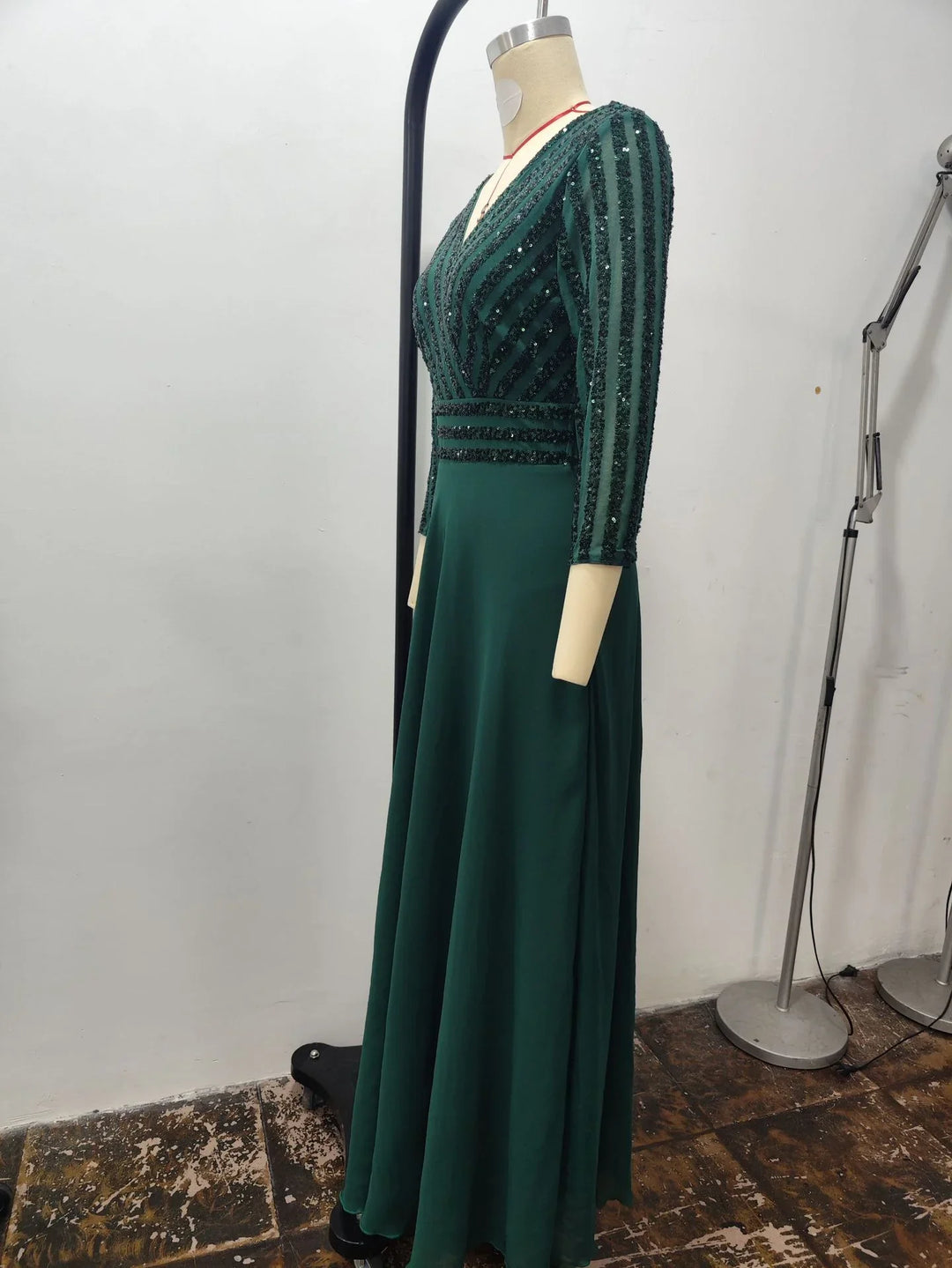 Elegant dark green formal gown with sequin striped bodice and three-quarter sleeves on mannequin